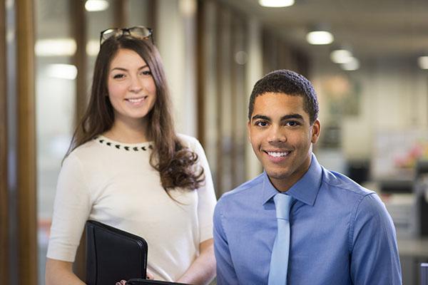 young man and woman stand in their new workplace smiling proudly to camera .